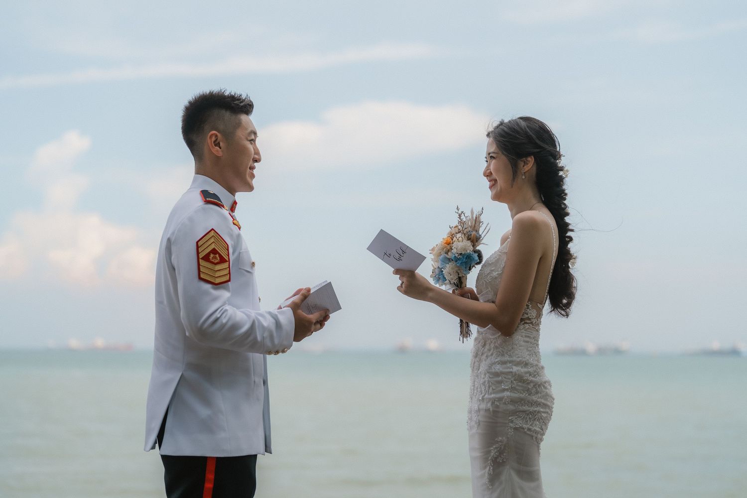 A couple exchanges vows during their seaside wedding ceremony with turquoise waters and cloudy skies in the background.