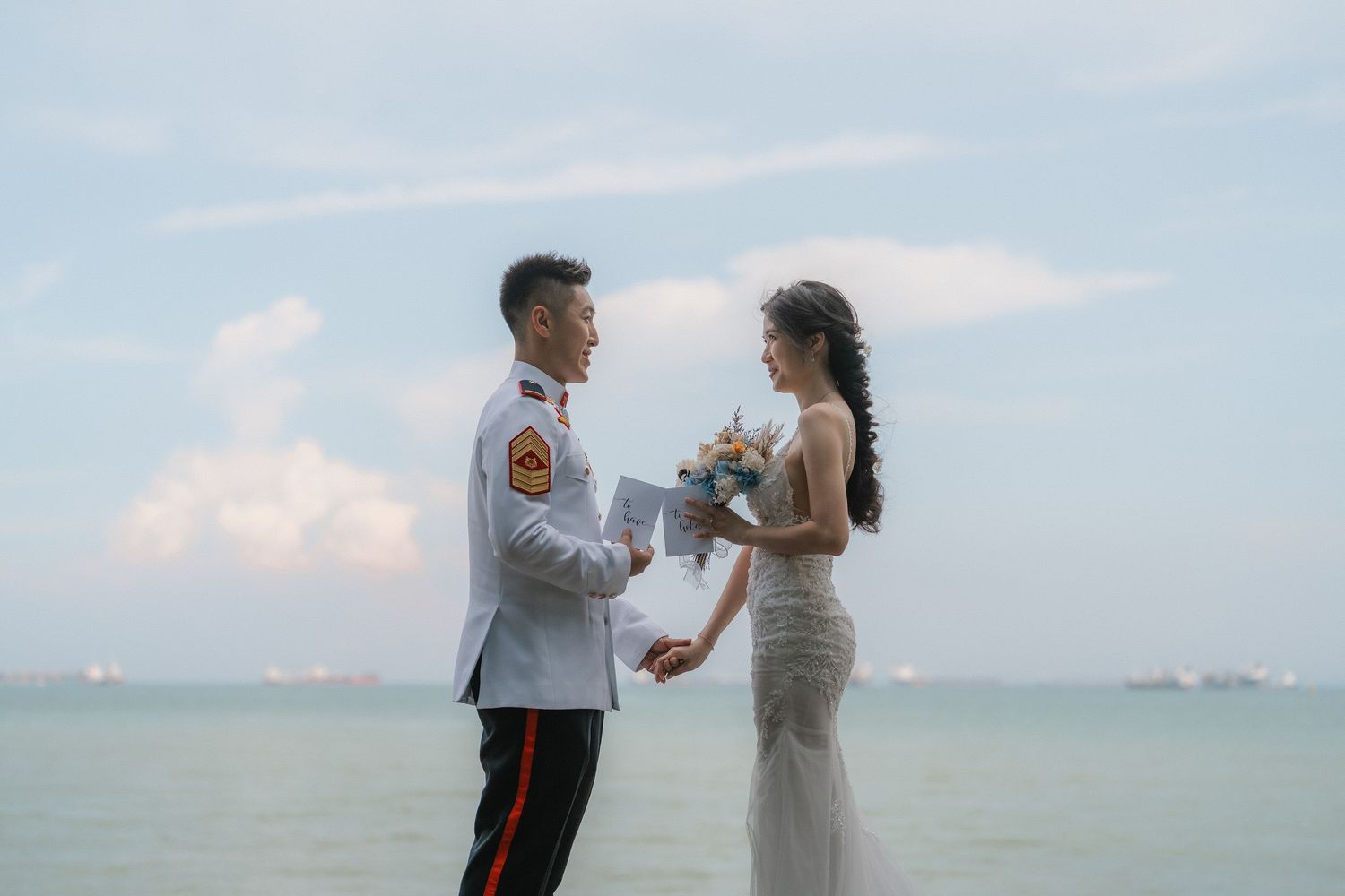 A couple in wedding attire stands together by the ocean during a romantic beachside ceremony.