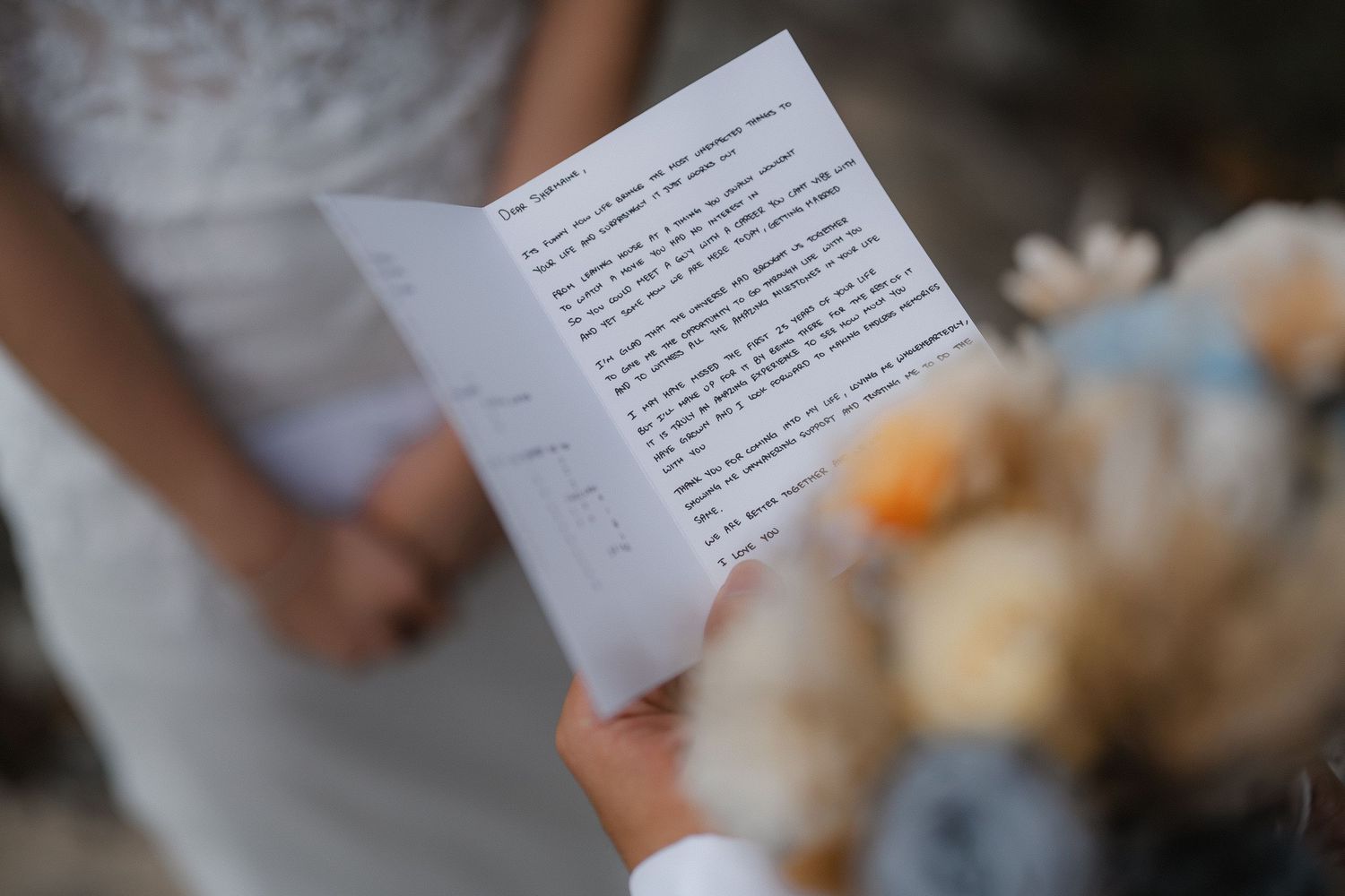 Someone in a white dress holds handwritten wedding vows on paper during an intimate ceremony.