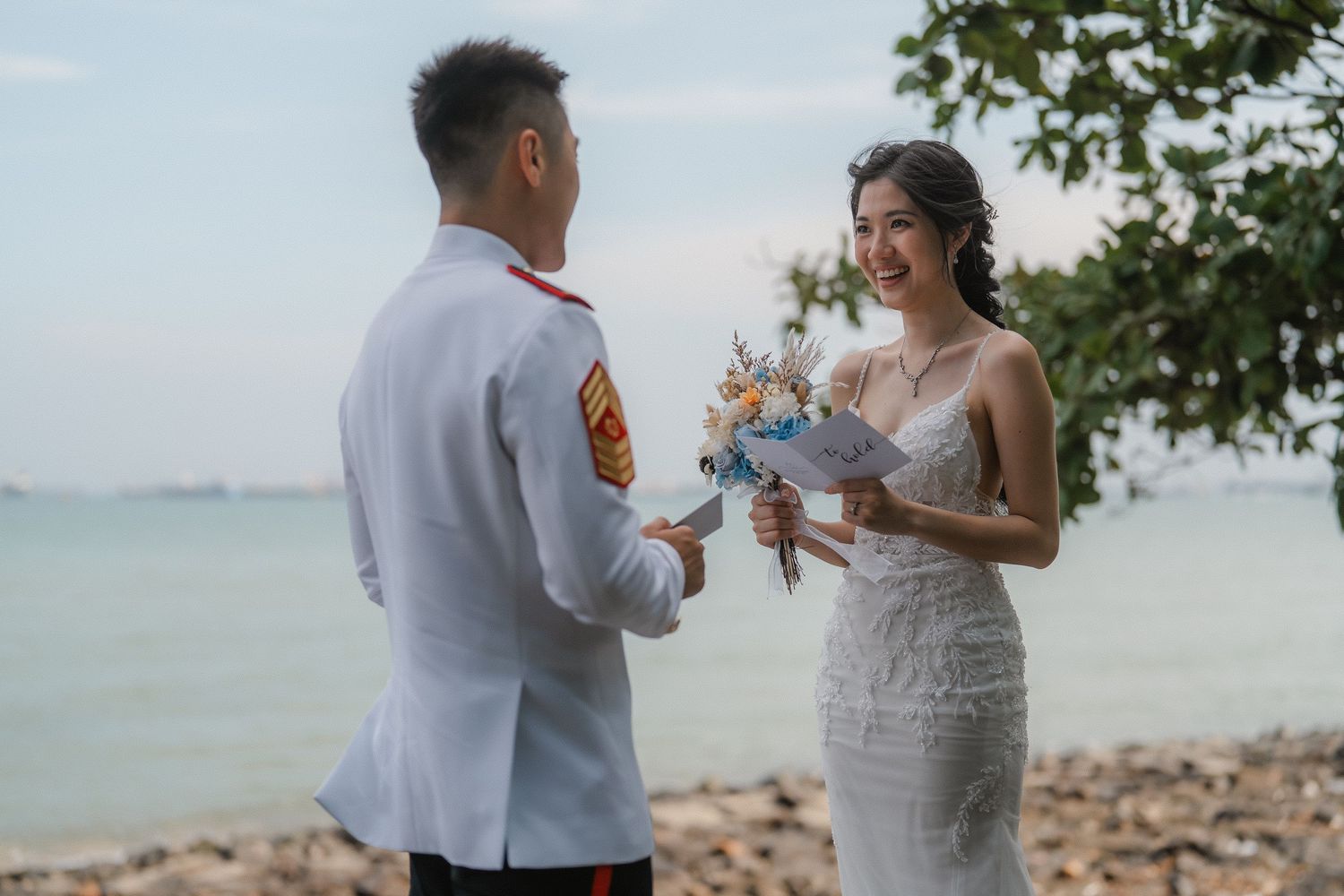 A couple shares a romantic moment during an outdoor beach wedding ceremony in elegant white attire.