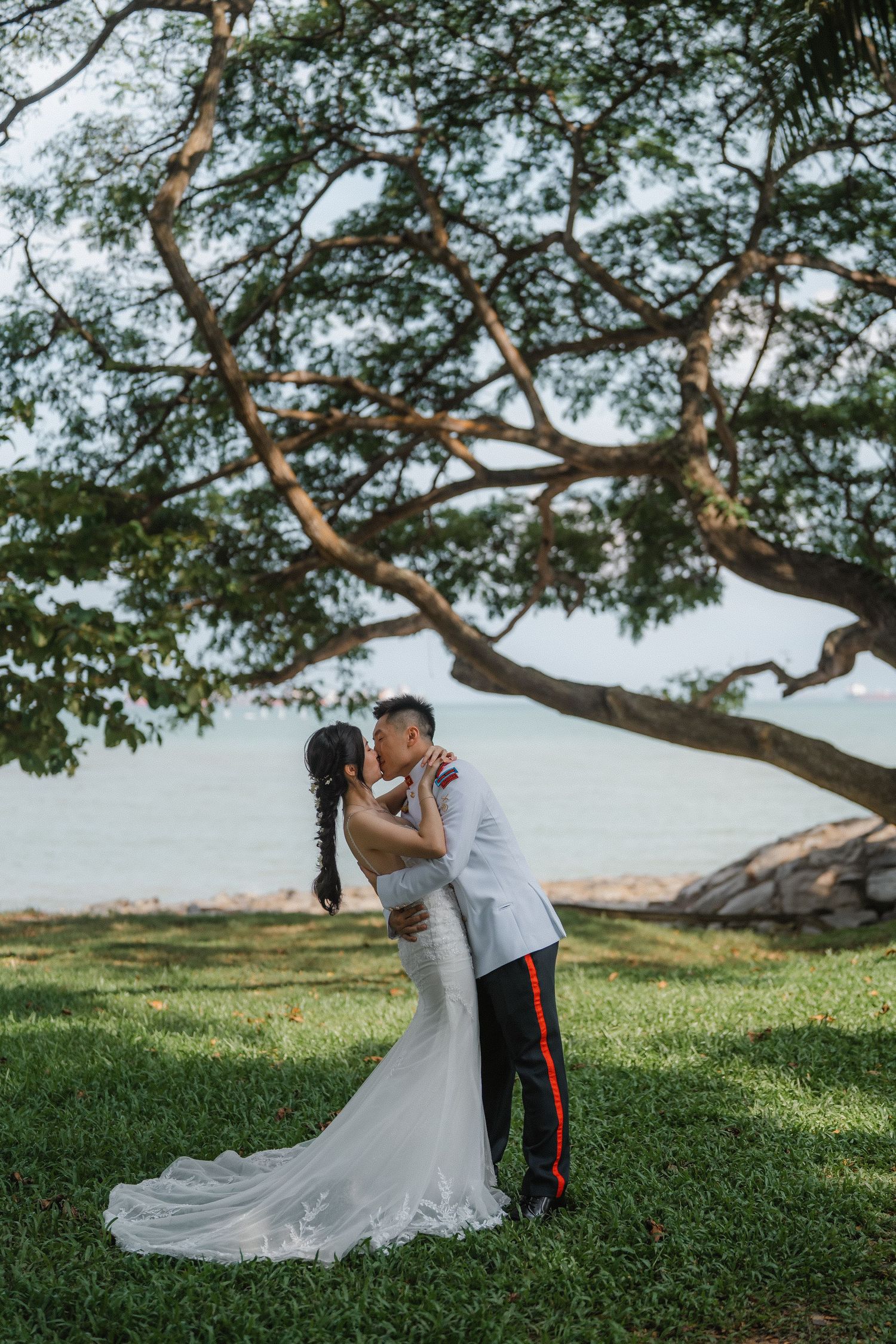 A romantic military wedding photo captures the couple sharing a kiss beneath a sprawling tree.