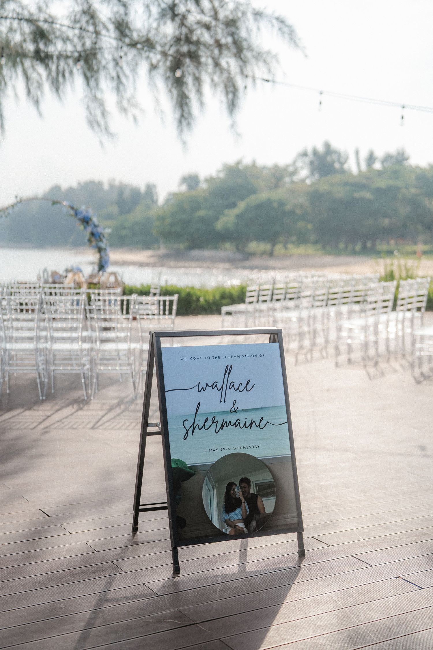 Welcome sign for a wedding ceremony setup with white chairs by the beach at sunset.
