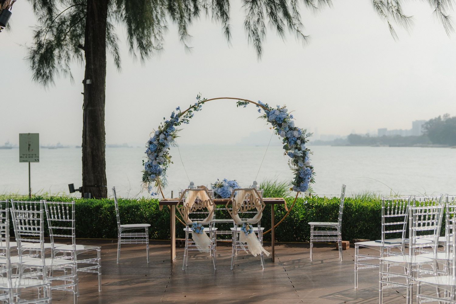 Elegant outdoor wedding ceremony setup with a floral arch and white chairs overlooking a serene waterfront view.