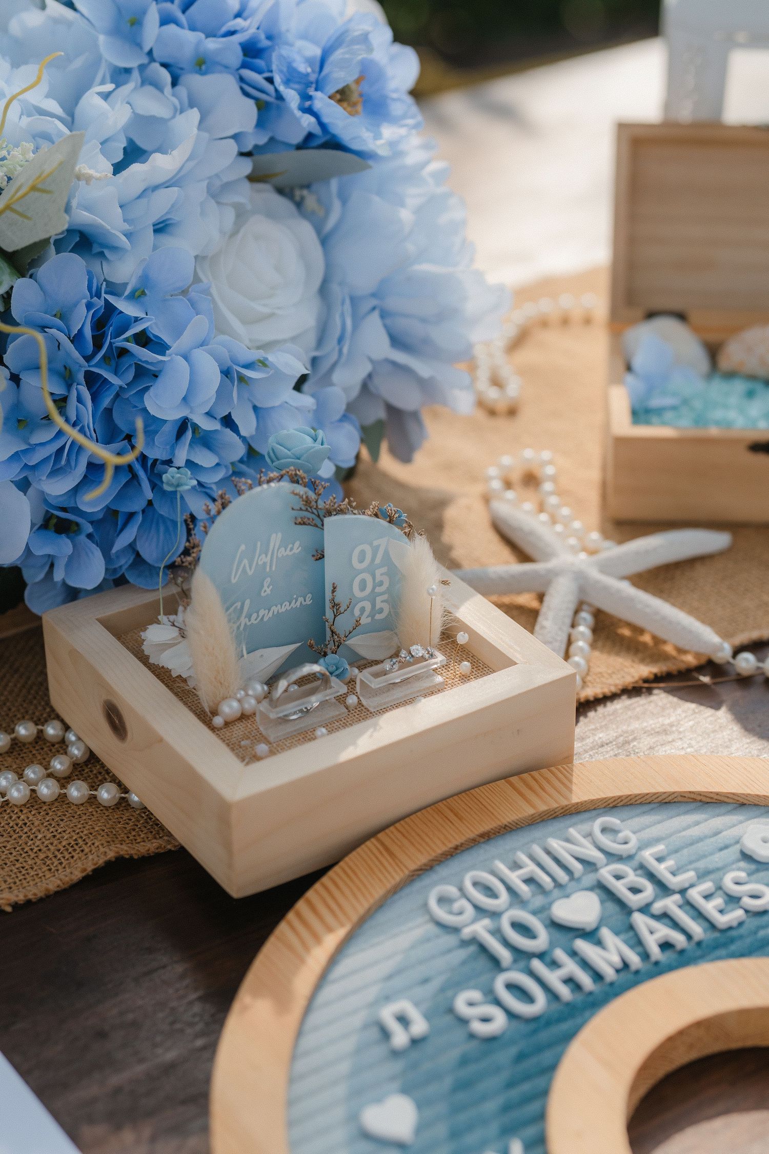 Light blue hydrangea flowers arranged in white wooden box with decorative coastal elements and soft blue glass jars.