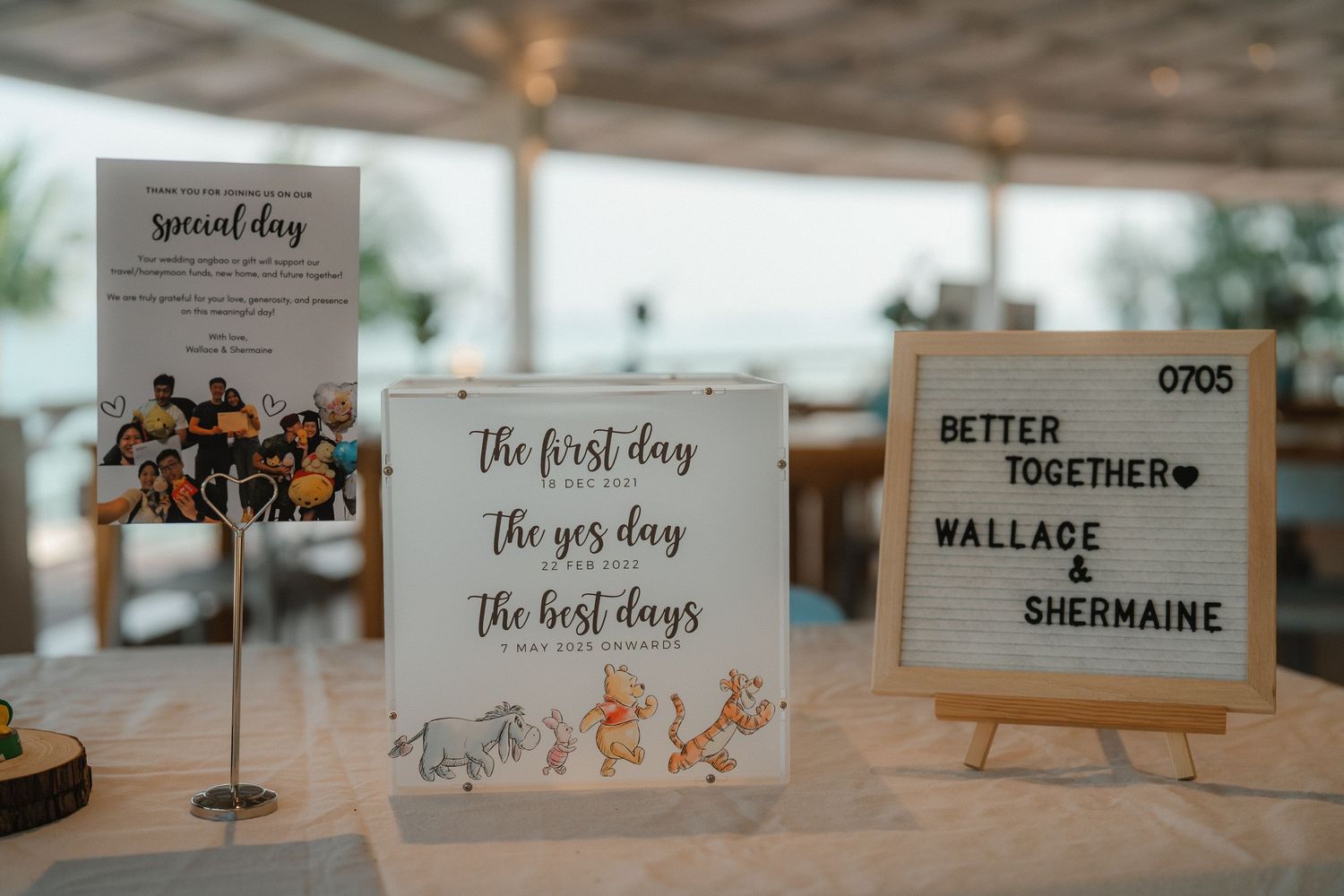 Three wedding reception table signs displayed on stands with rustic lettering and decor at a light-filled venue.
