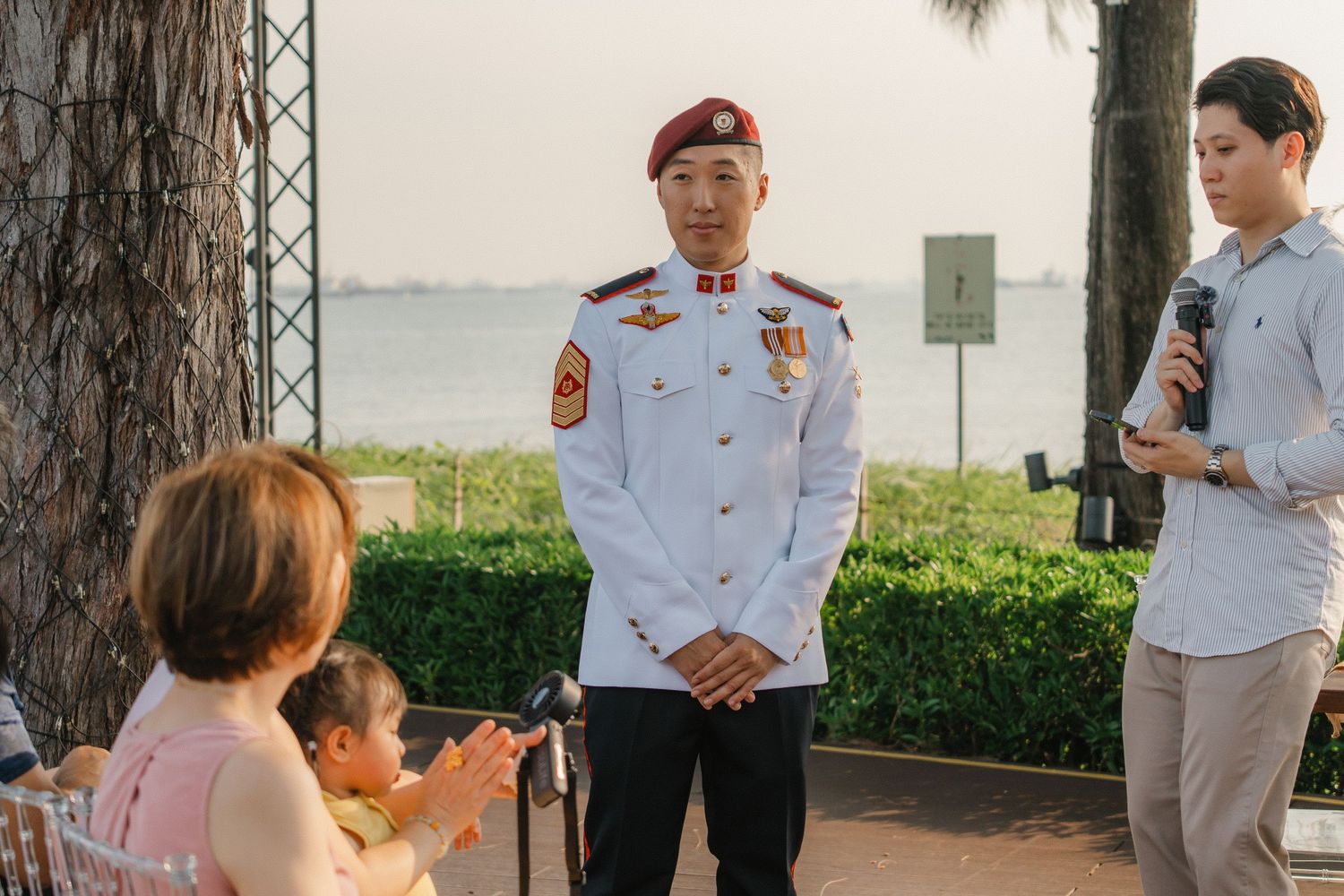 Military personnel in dress uniforms gather outdoors during a formal ceremony on a sunny day.
