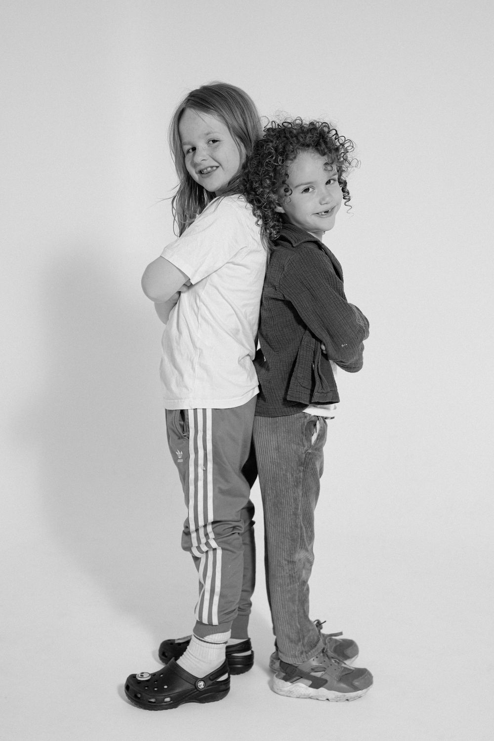 Two children stand back-to-back in casual wear for black and white portrait