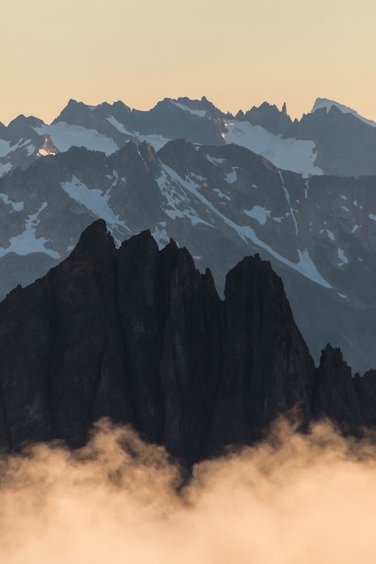Silhouetted mountain peaks rise dramatically against a misty sunset sky with low-lying clouds in the foreground.