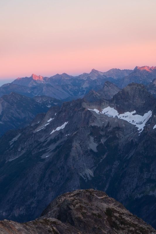 Majestic mountain peaks silhouetted against a pink and purple sunset sky with snow patches visible on distant ridges.