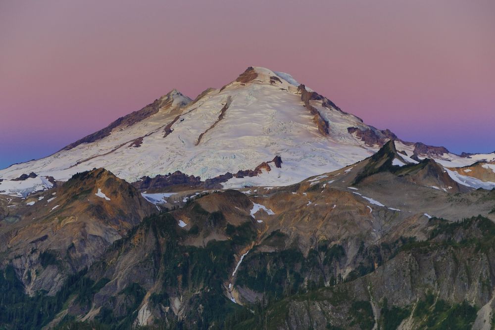 Snow-capped Mount Baker reflects golden alpenglow during sunset in North Cascades National Park, Washington.