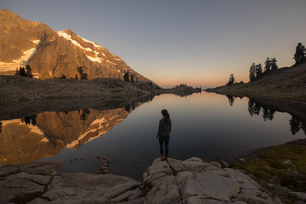 A serene mountain lake reflects snow-capped peaks during golden hour in an alpine landscape.