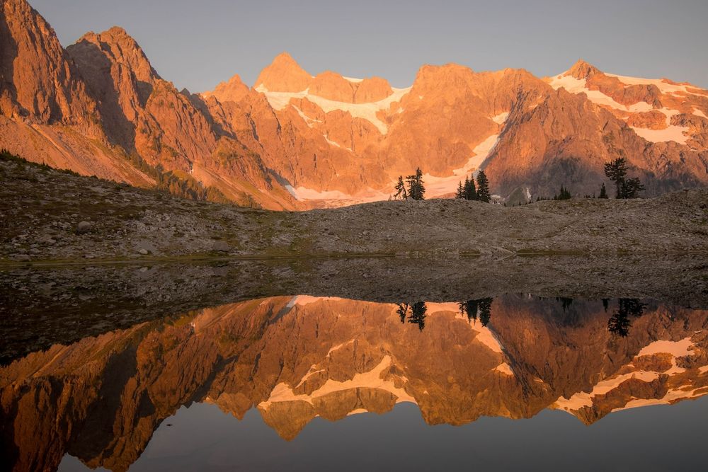 Dramatic mountain peaks glowing orange at sunset with reflections in a still alpine lake.