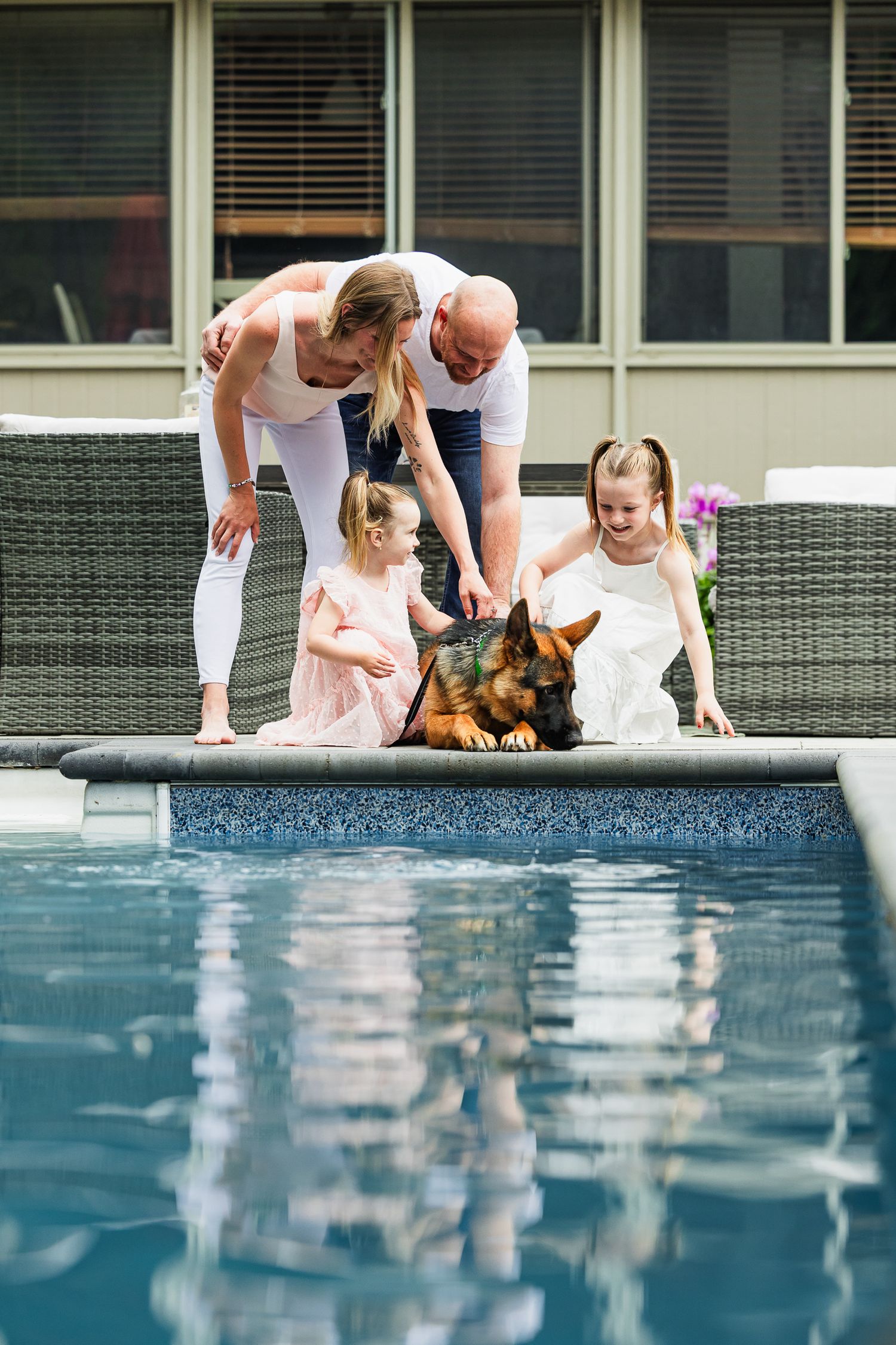Family and their German Shepherd dog gathered at the edge of a swimming pool on a sunny day.