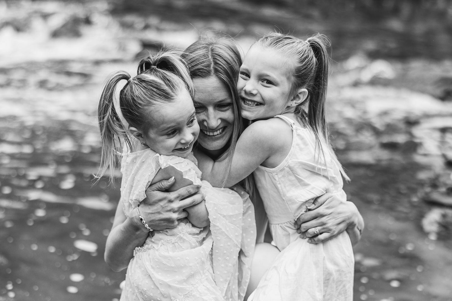 Three people share a warm embrace while standing in a stream.
