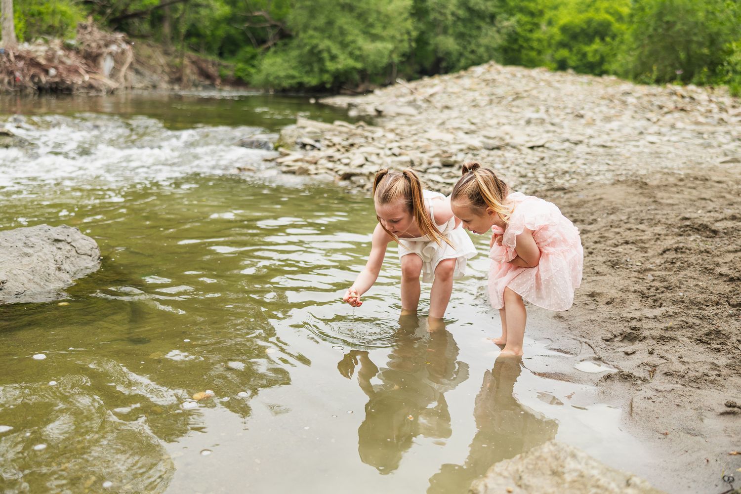 Children playing near the edge of a rocky stream on a summer day exploring nature together.