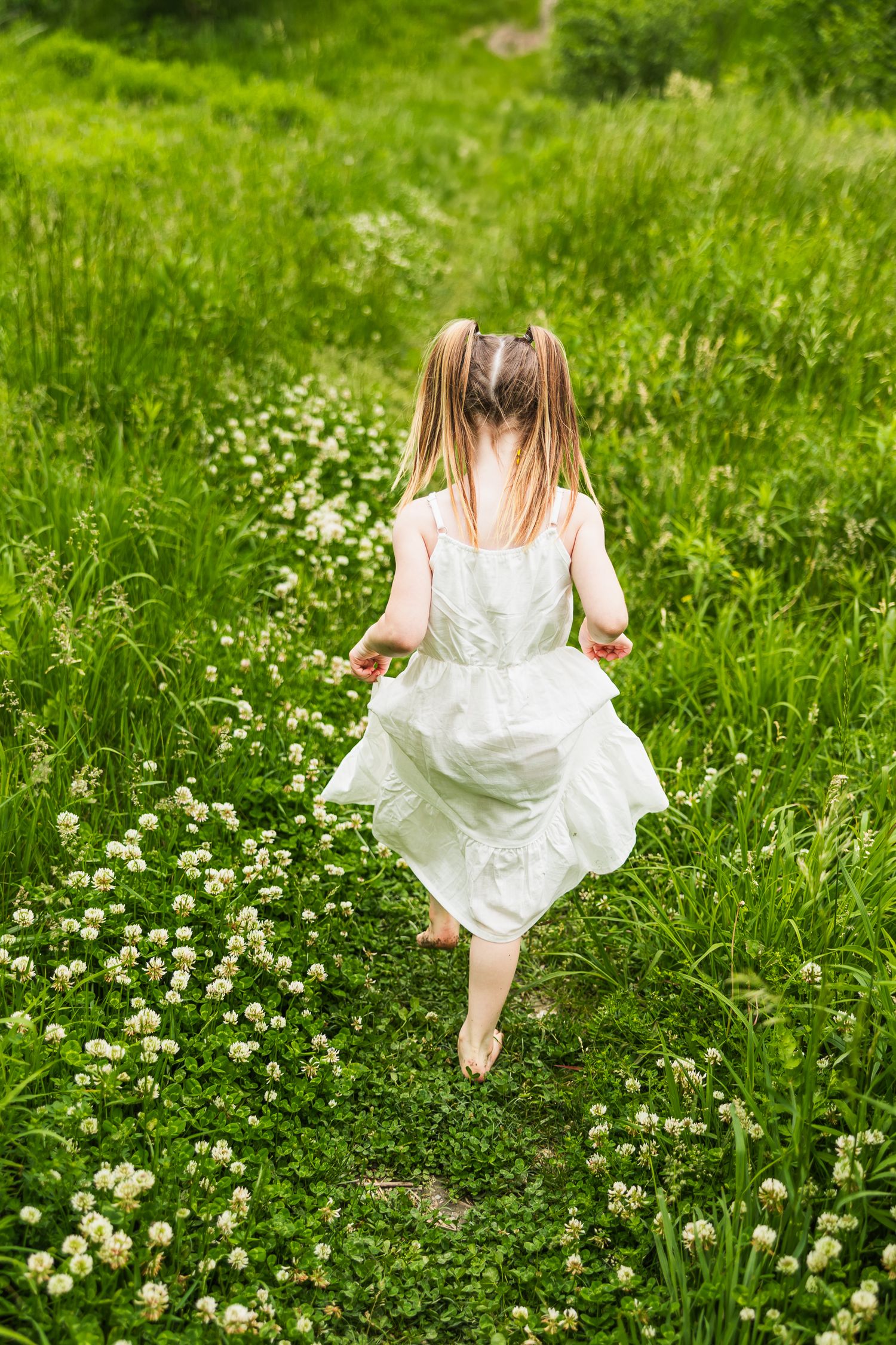 A person in a white dress dances through a field of blooming flowers on a sunny day.