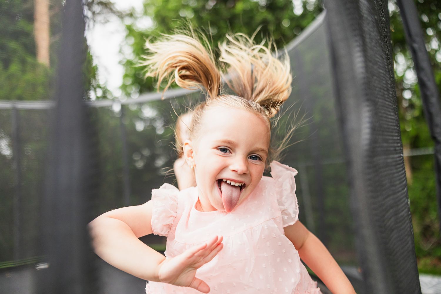 Child jumping with joy on a trampoline wearing a pink dress with ruffles.