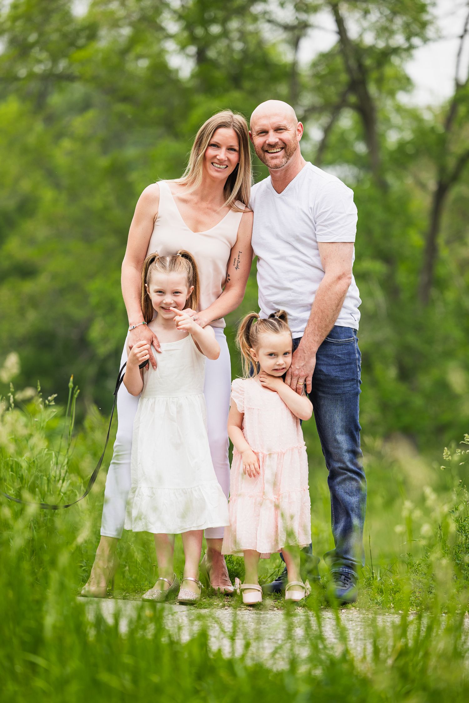 A family of four poses together outdoors in a lush green meadow on a bright summer day.