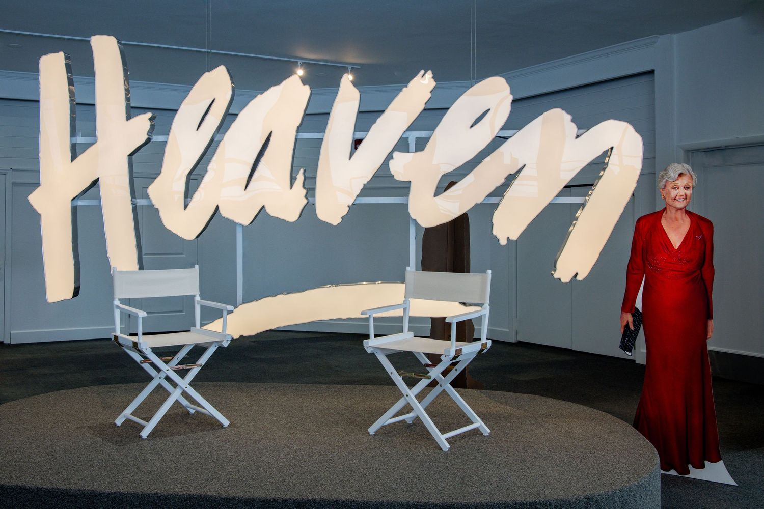 Three white director's chairs arranged in front of a wall display illuminated with text and lighting elements.