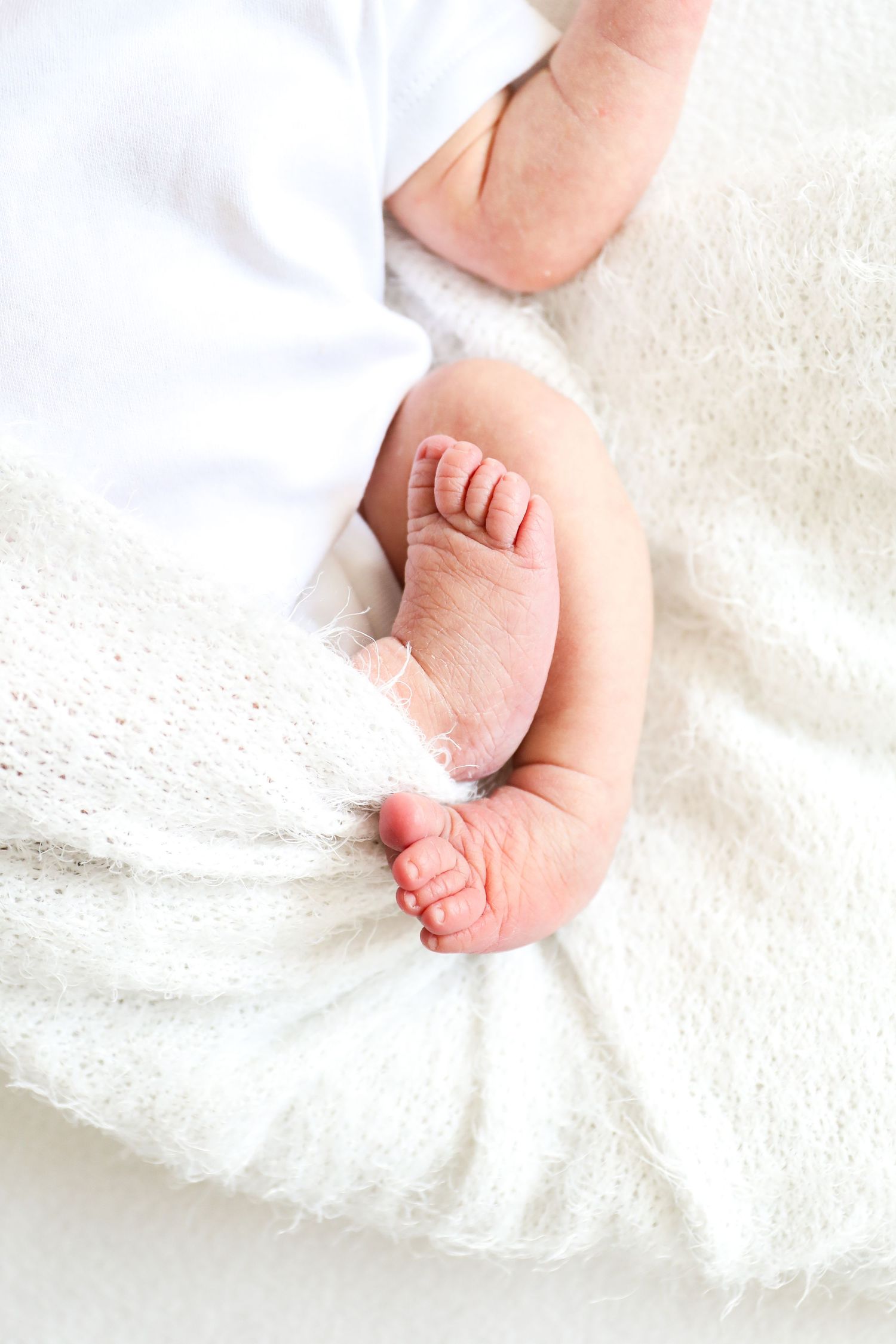 Close-up of tiny newborn baby feet wrapped in soft white blanket against light textured background, during newborn shoot in Nottingham
