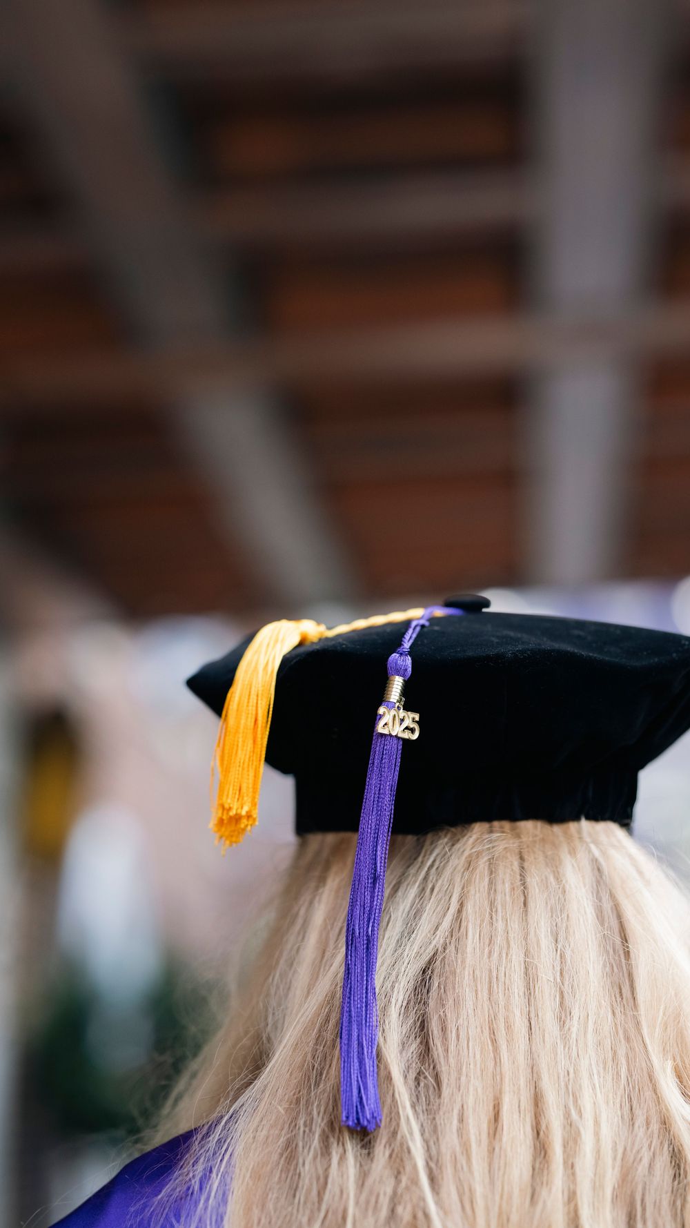 Close-up view of a graduation cap with gold and purple tassels adorning it against a blurred background.