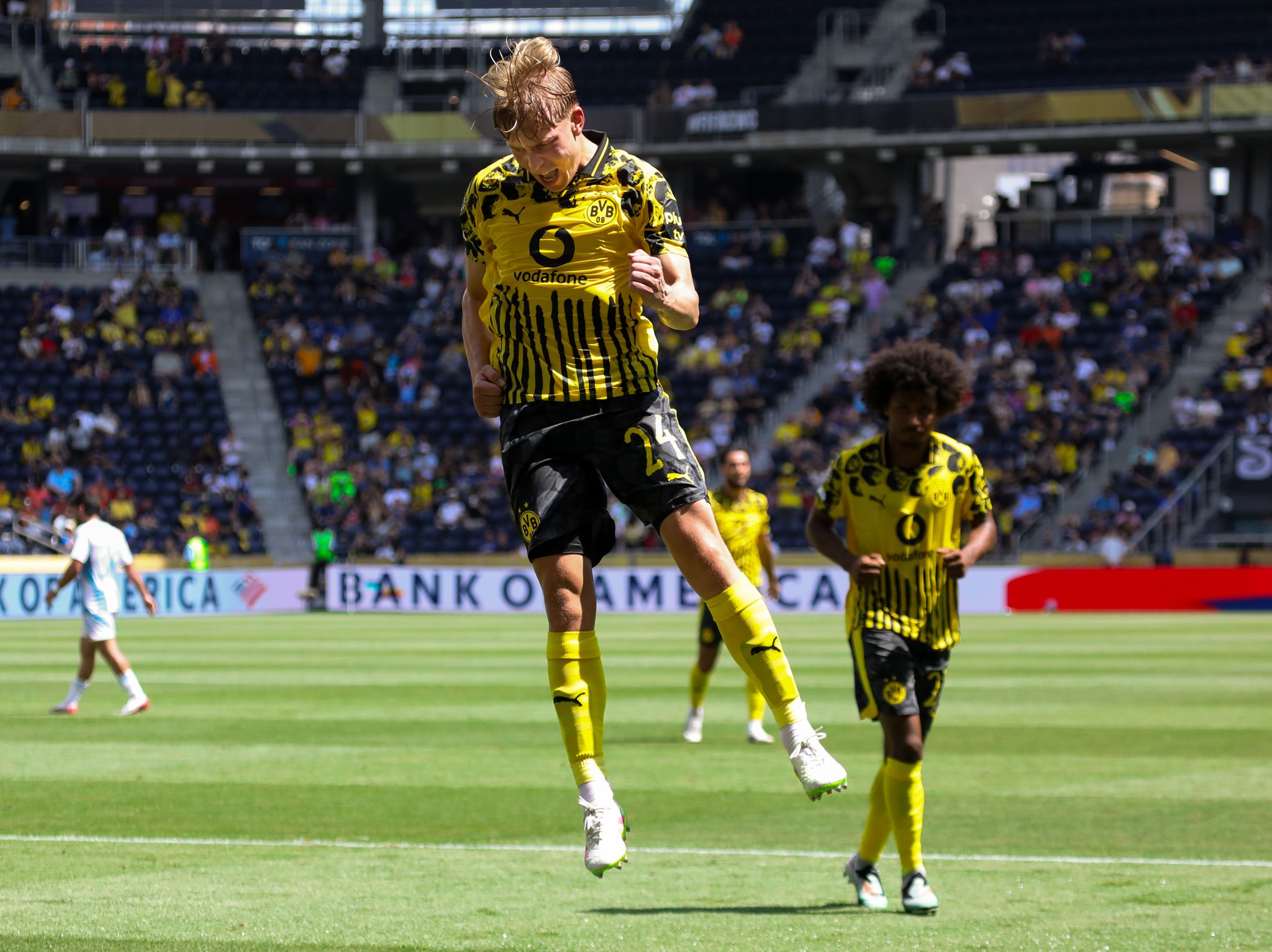 Soccer player in yellow and black striped uniform celebrates after scoring during professional match at stadium.