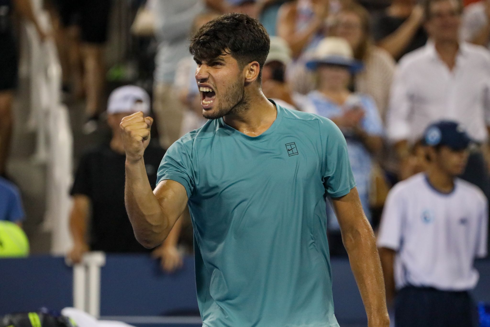 Tennis player in teal shirt celebrates during a match with emotional fist pump and victory shout on court.