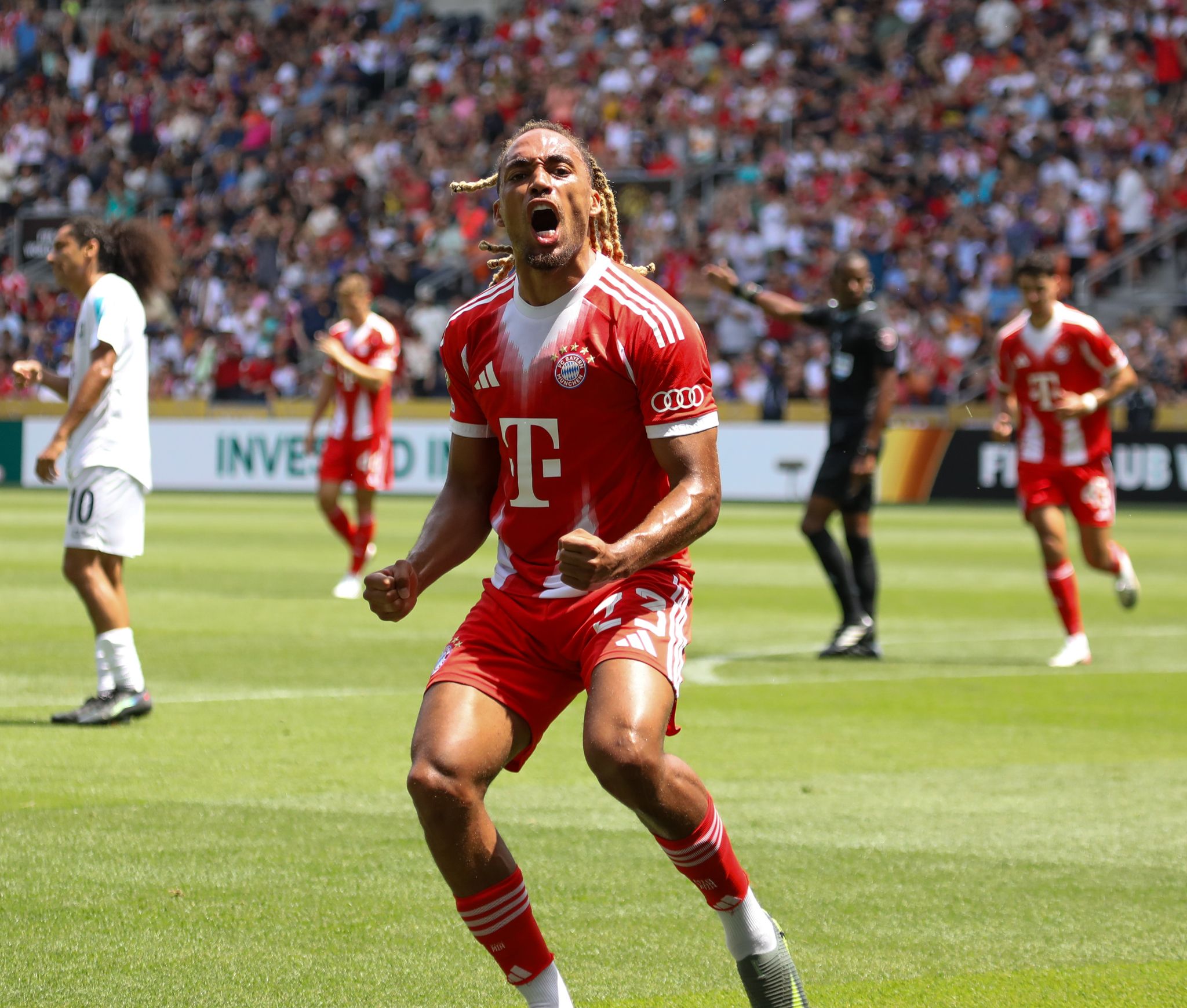 Professional soccer player in a red Bayern Munich jersey reacts during a match at a crowded stadium.