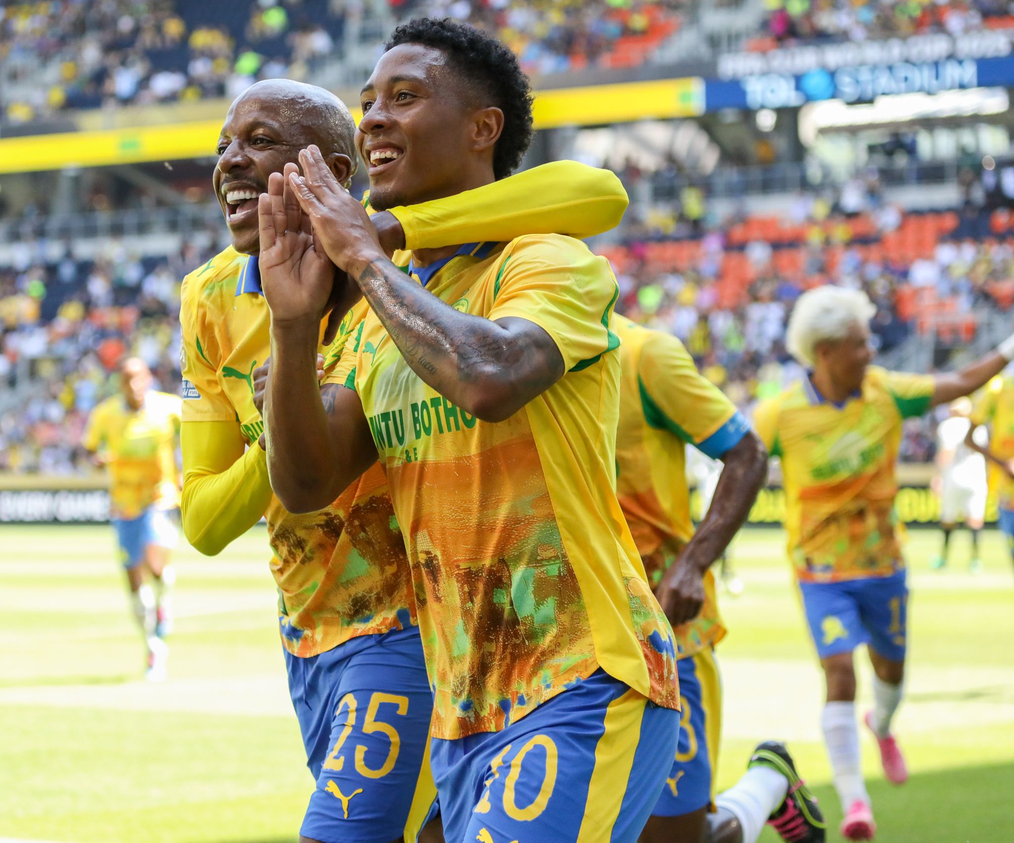 Soccer players in yellow jerseys celebrating a goal with joyful expressions and raised arms during a match.