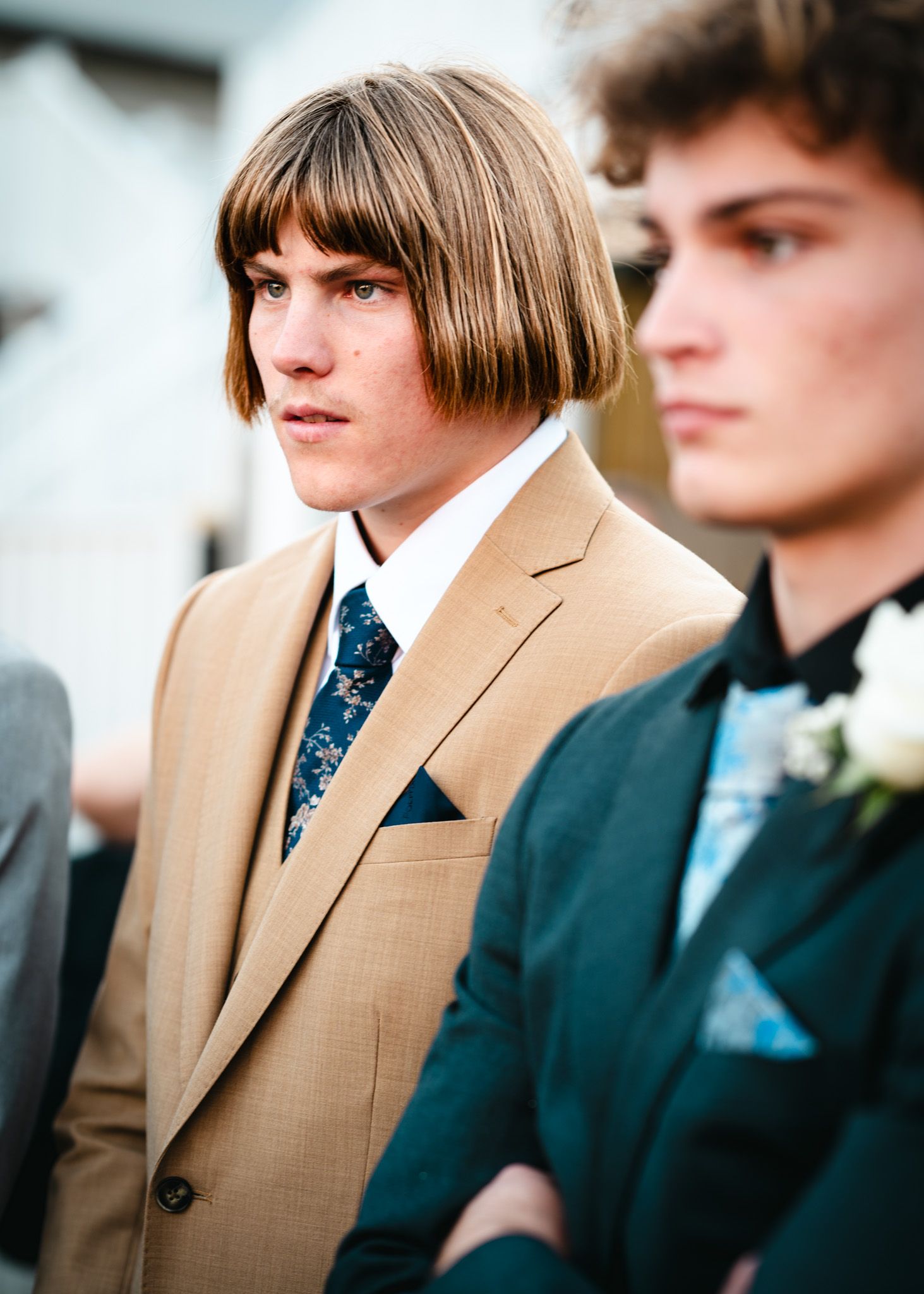 Two young men in formal suits at their Pre-Formal event stand close together in profile view.