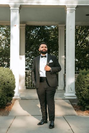 Classic groom portraits in a black tuxedo standing beneath white architectural columns.