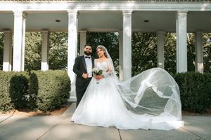 Wedding couple photographed under white columns with flowing veil catching the breeze.