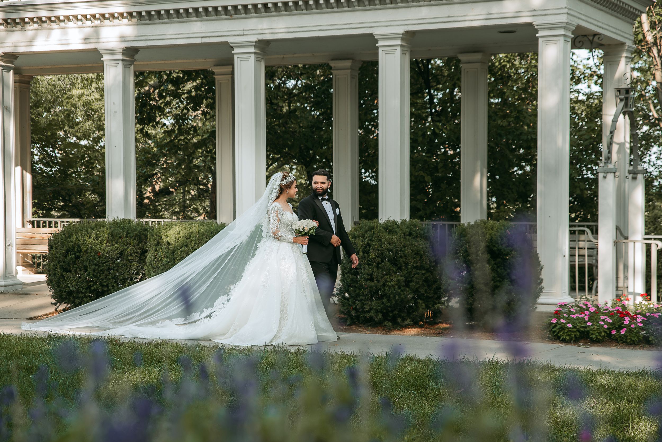 Elegant wedding portraits captured along a white columned veranda with purple flowers in foreground.