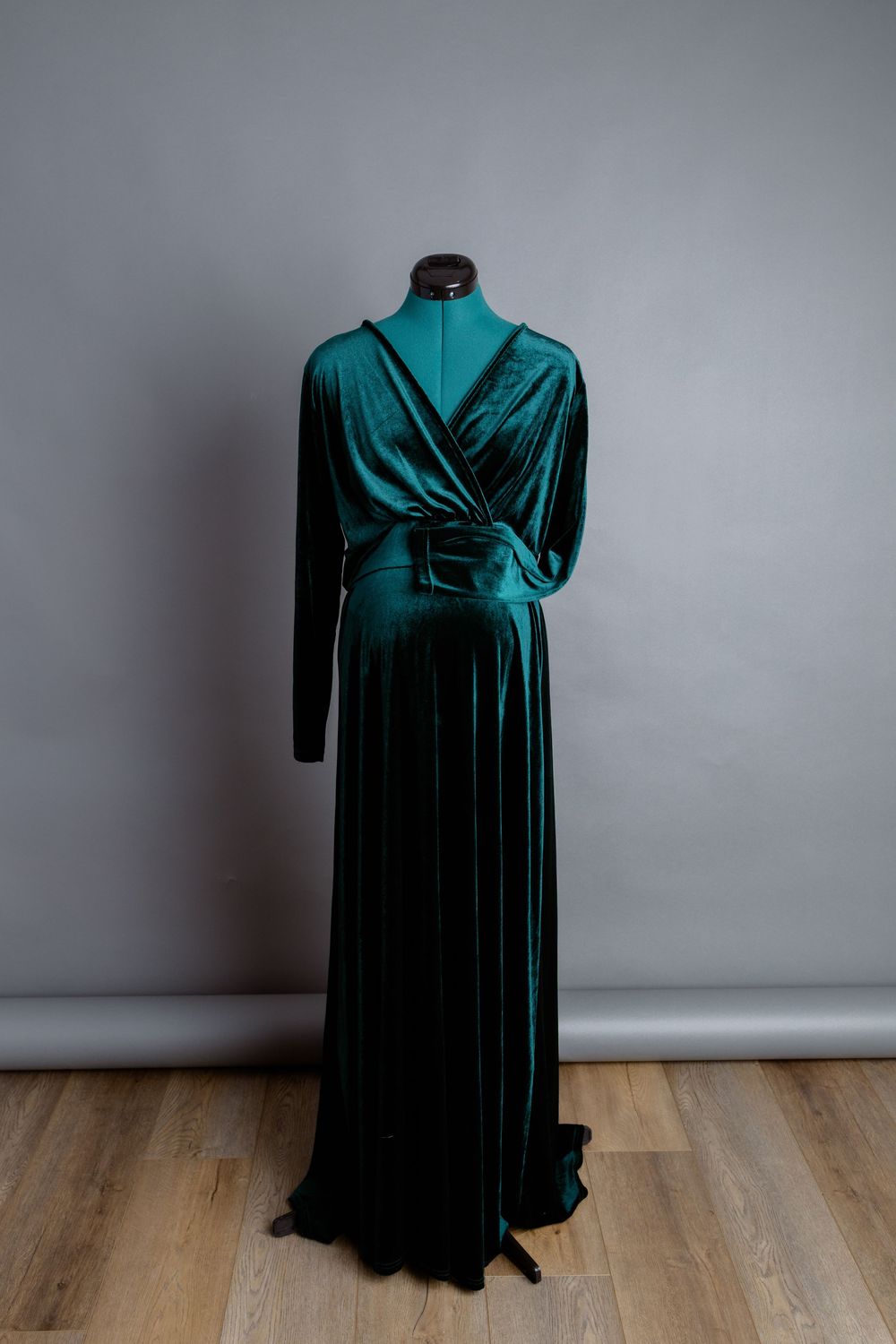 Elegant emerald green velvet wrap dress on mannequin against grey wall.