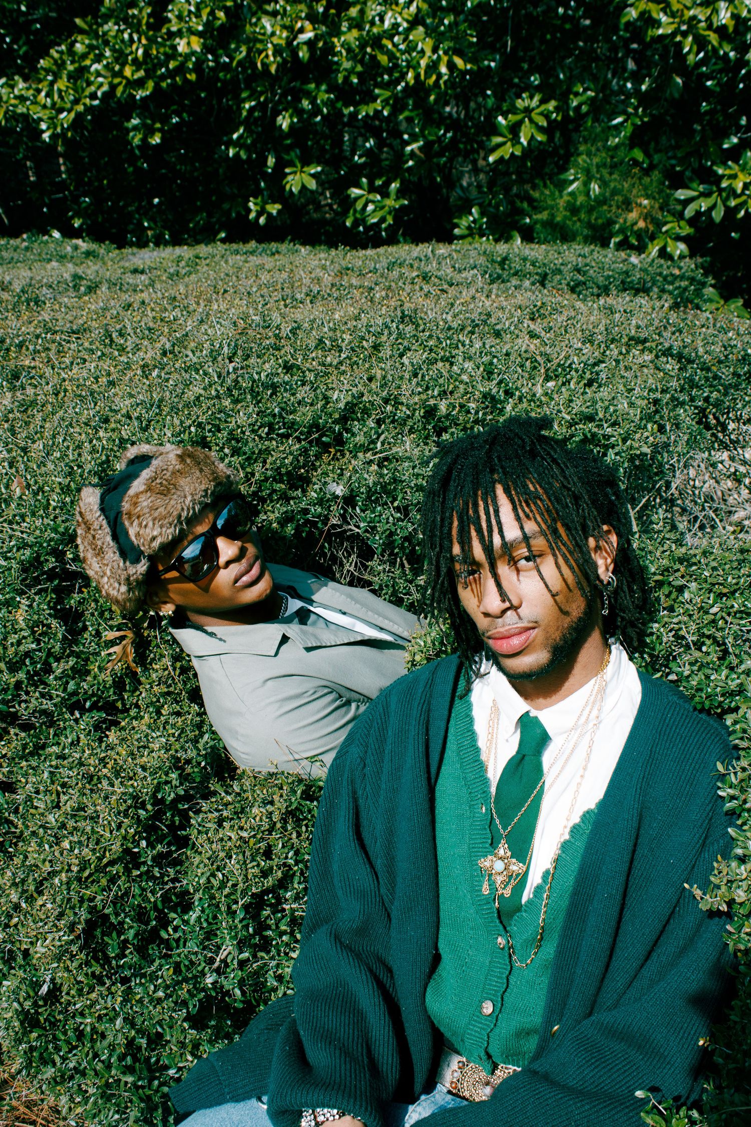 Two people in casual and formal attire pose outdoors against green foliage.