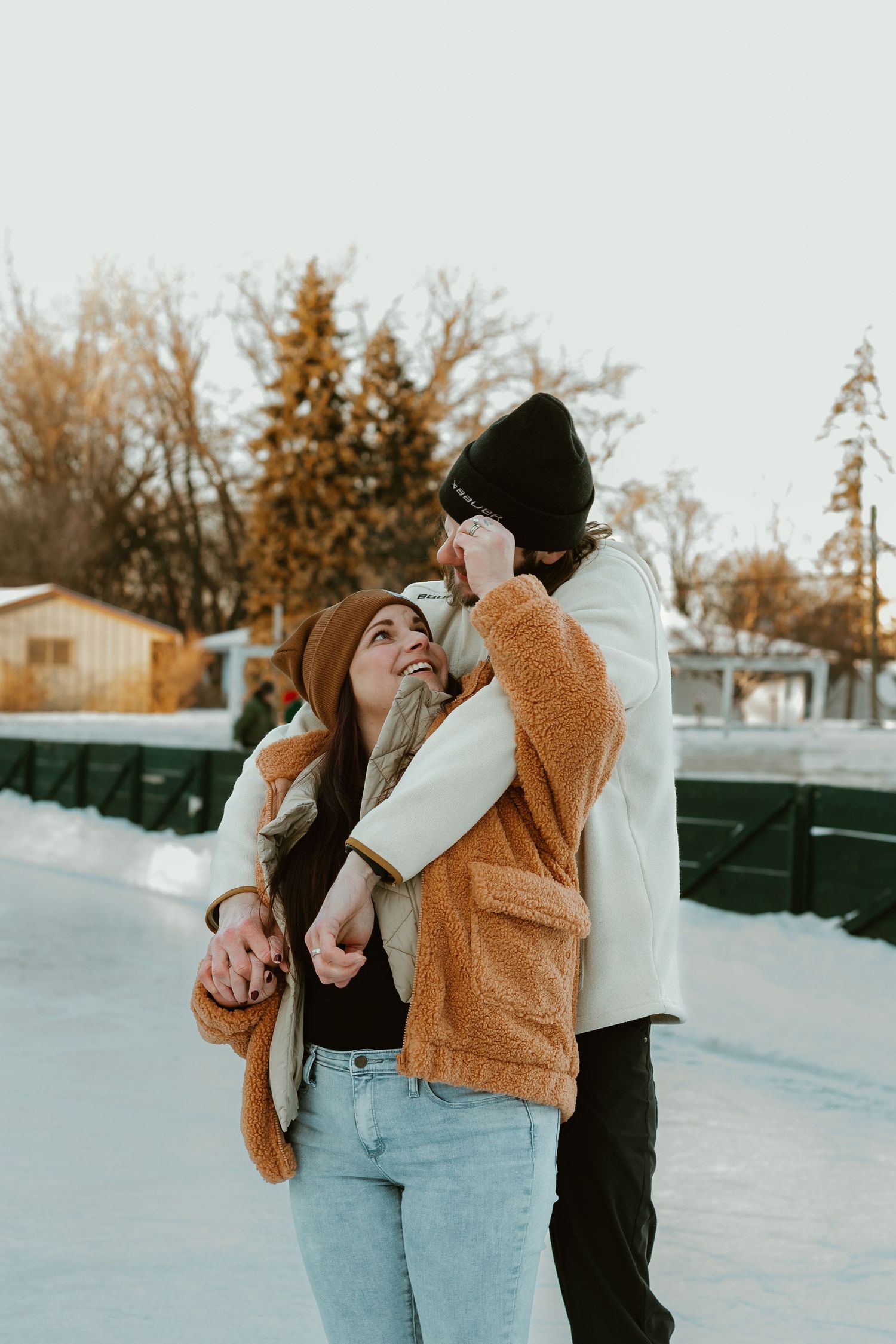 A couple embraces while ice skating outdoors on a winter afternoon in warm cozy outerwear.