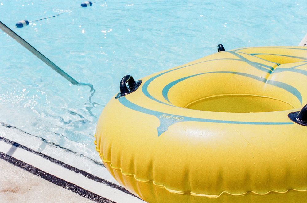 A bright yellow inflatable pool tube sits at the edge of a swimming pool with crystal clear blue water.