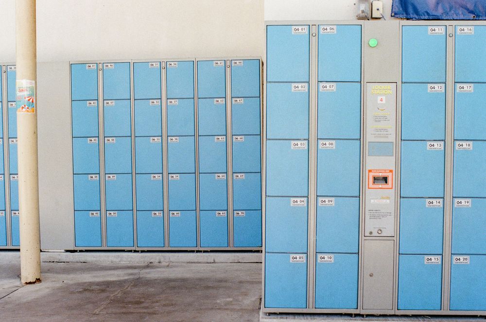 Blue metal storage lockers lined up against a wall in a public facility with numbered compartments.
