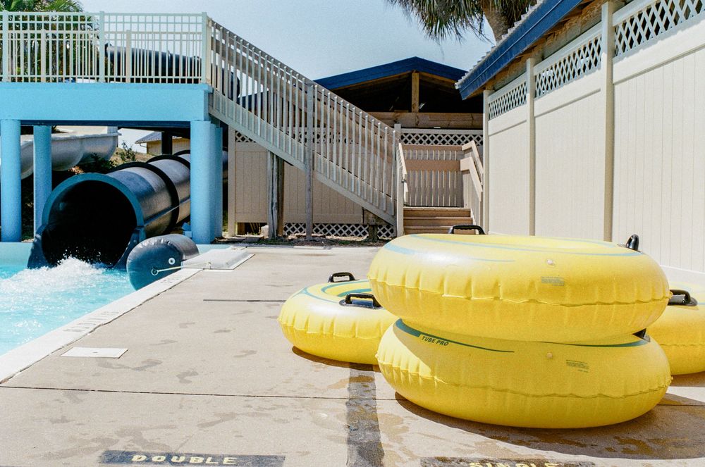 Yellow inner tubes lay next to a water slide at a pool area with white railings and blue accents.