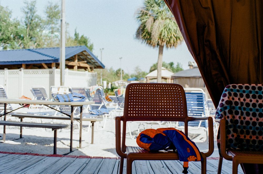 A beach chair and towel on a wooden deck overlooking lounge chairs and palm trees on a sunny Florida beach.