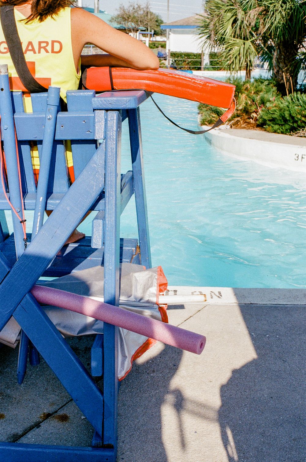 A blue lifeguard chair overlooks a swimming pool with orange rescue equipment visible.