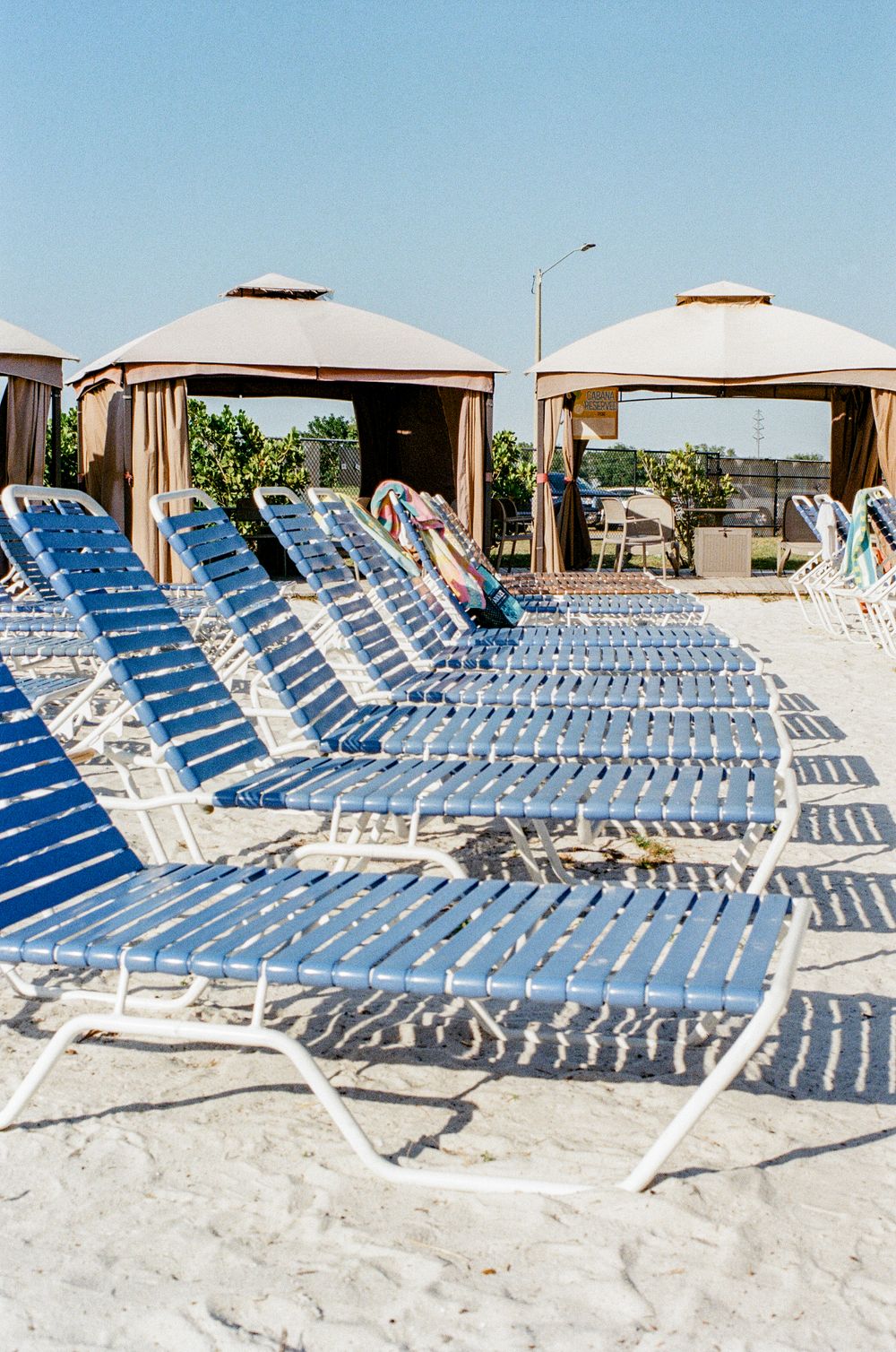 Rows of blue and white lounge chairs lined up under beige cabanas on a sunny beach.