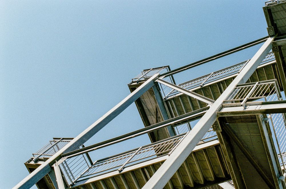 Looking up at modern architectural details of metal beams and railings against a bright blue sky.