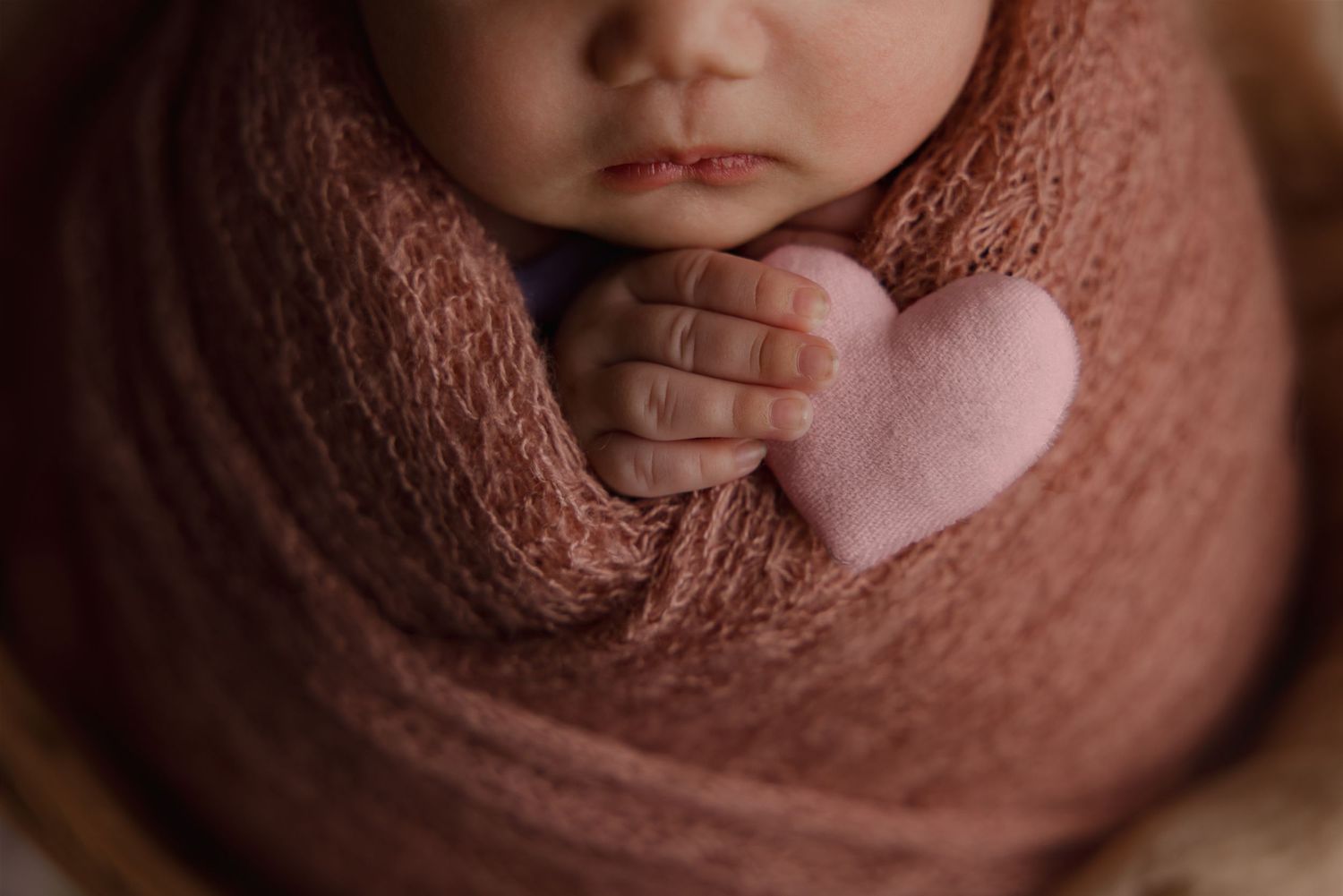Newborn baby swaddled in blanket holding felt heart in hands