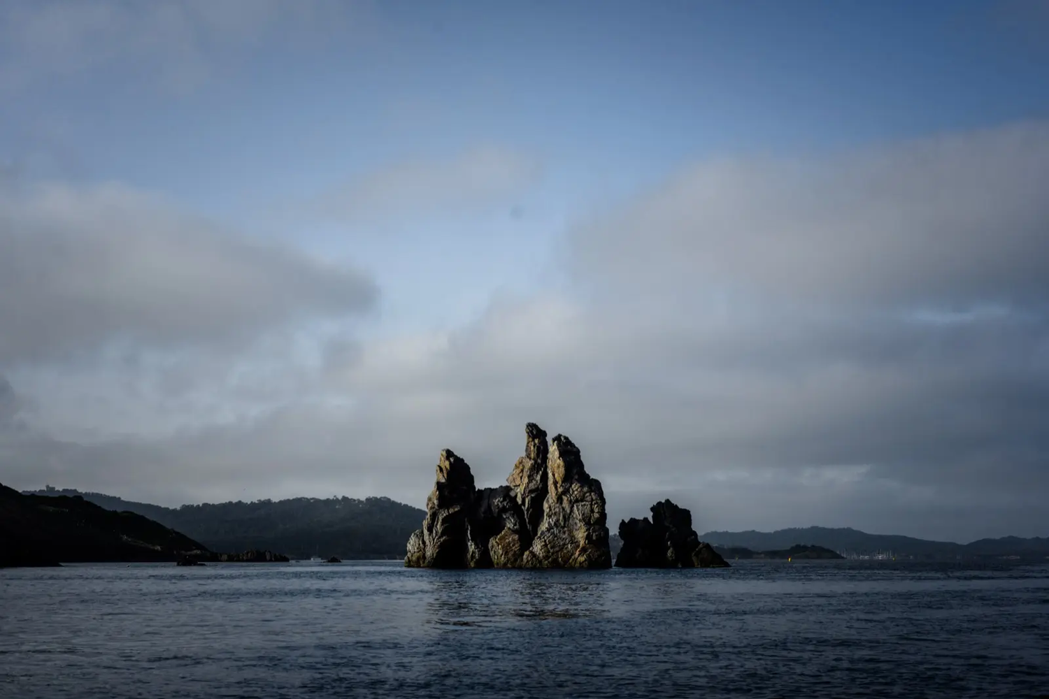 Formation rocheuse émergente de la mer sous un ciel nuageux, en paysage côtier.