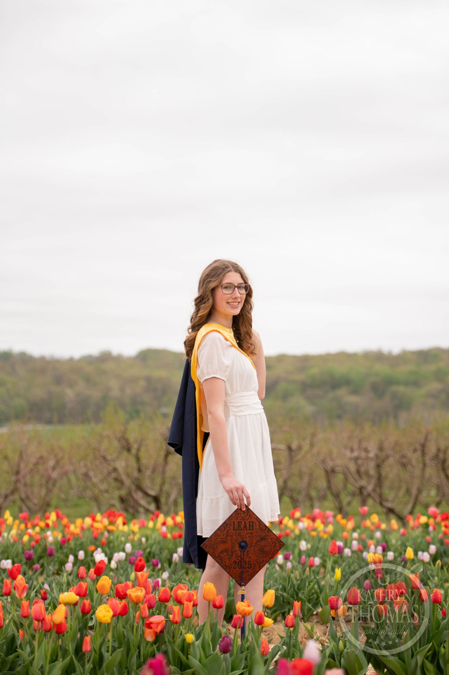 A beautiful portrait in a vibrant tulip field with a white dress and brown bag against a cloudy sky.