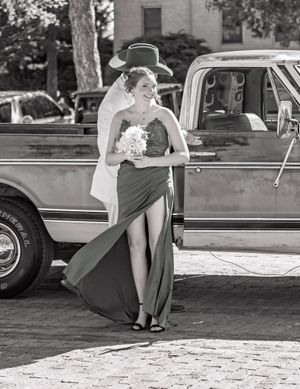 Retro-style black and white photo of someone in a flowing dress posing beside a vintage pickup truck.