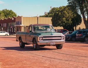 Classic Chevrolet C10 pickup truck parked in a town square parking lot on a sunny day.
