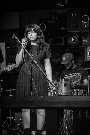 Black and white photo of a singer performing on stage with a microphone and speakers in the background.