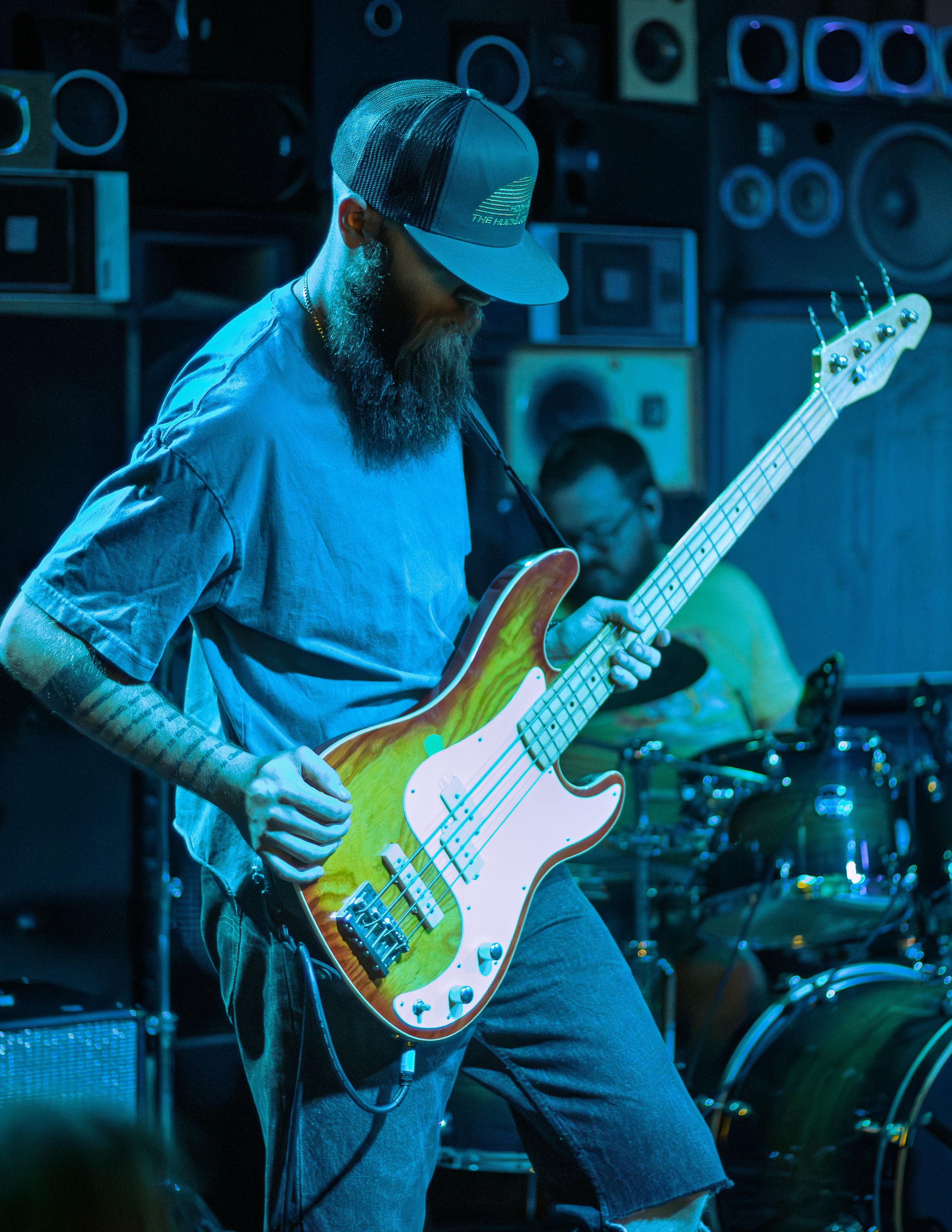 A bassist performs on stage with a green and white bass guitar under blue lighting during a live concert.